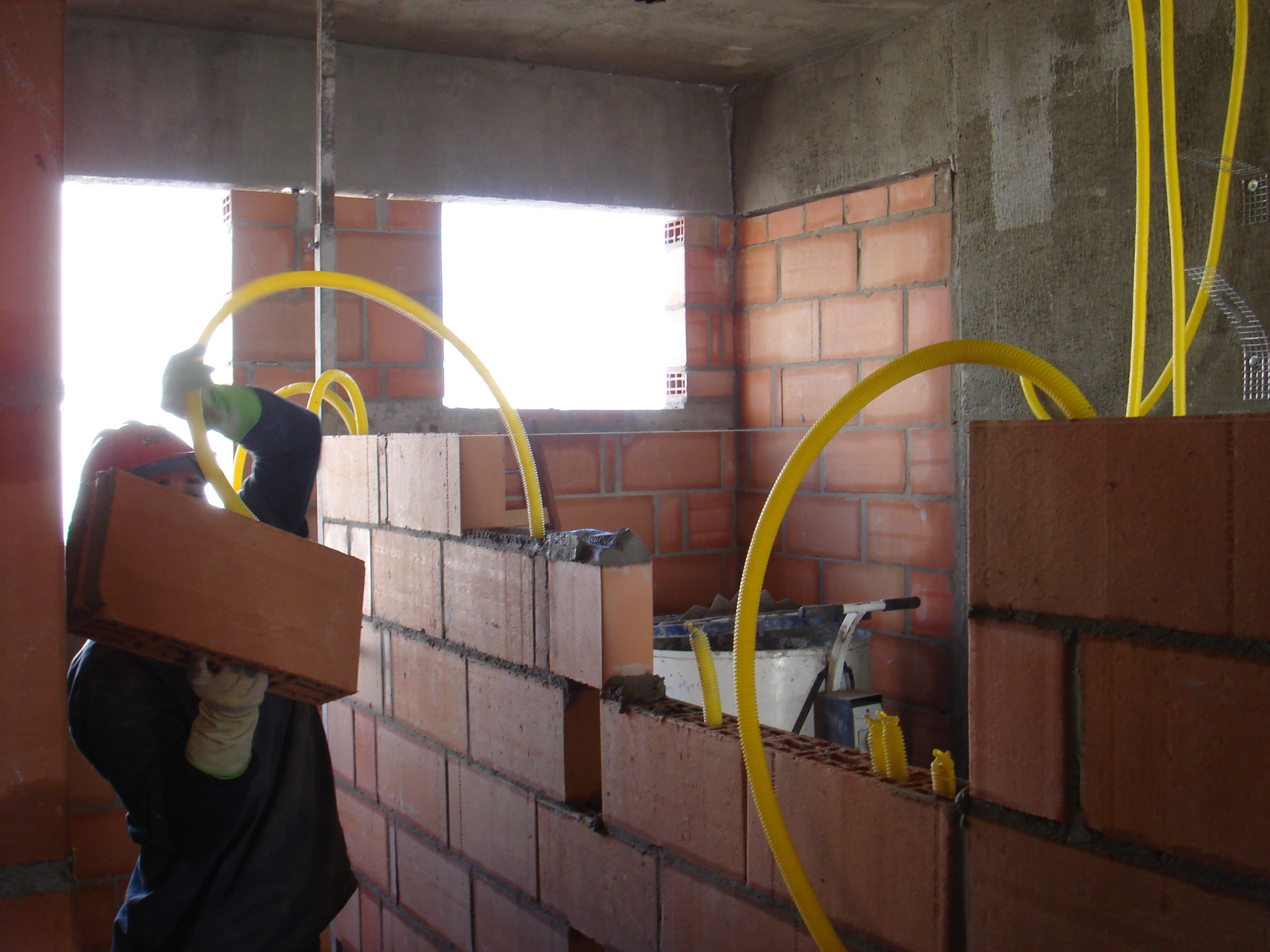 Pedreiro assentando blocos cerâmicos com instalações elétricas já embutidas na parede